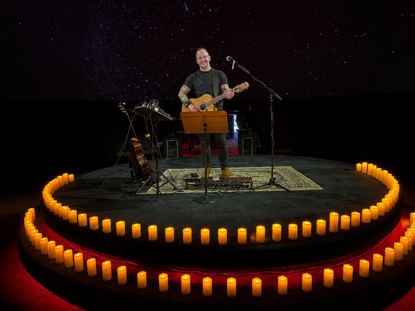 The performer at centre stage encircled by a full ring of candles, one for every seat, beneath a projected starfield at TELUS World of Science - Edmonton